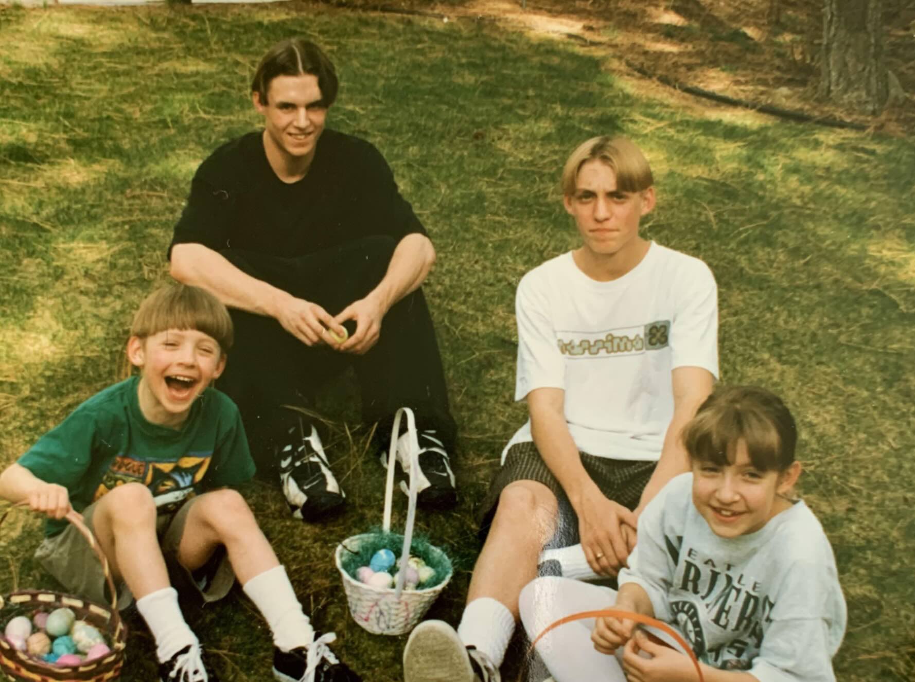 Two young men and two children sitting on a grassy lawn with Easter baskets.