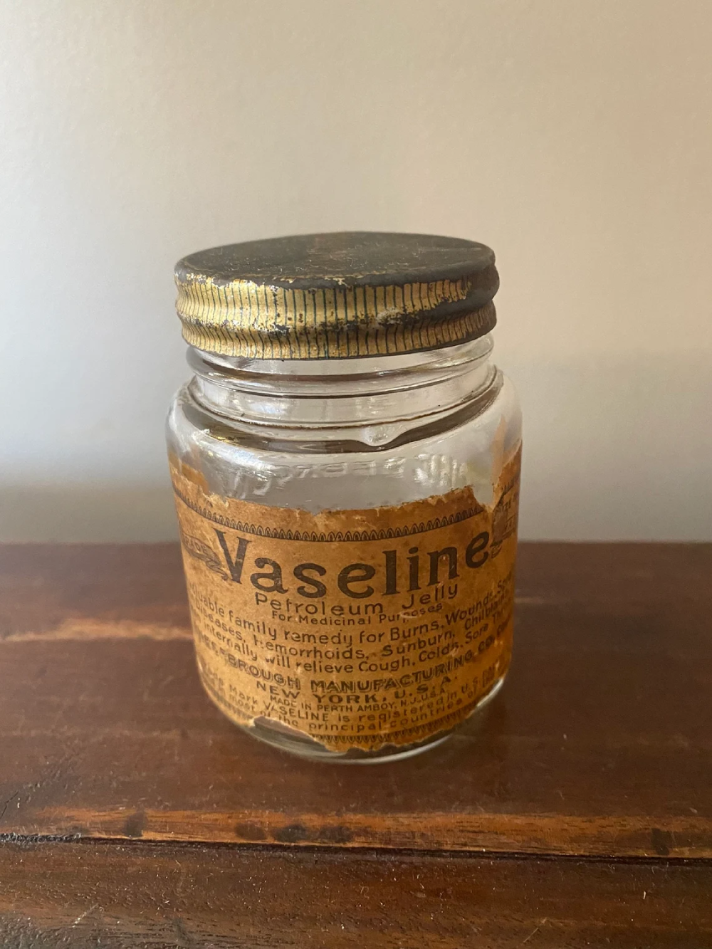 Vintage empty Vaseline Petroleum Jelly glass jar with a worn paper label and a metal screw-top lid.