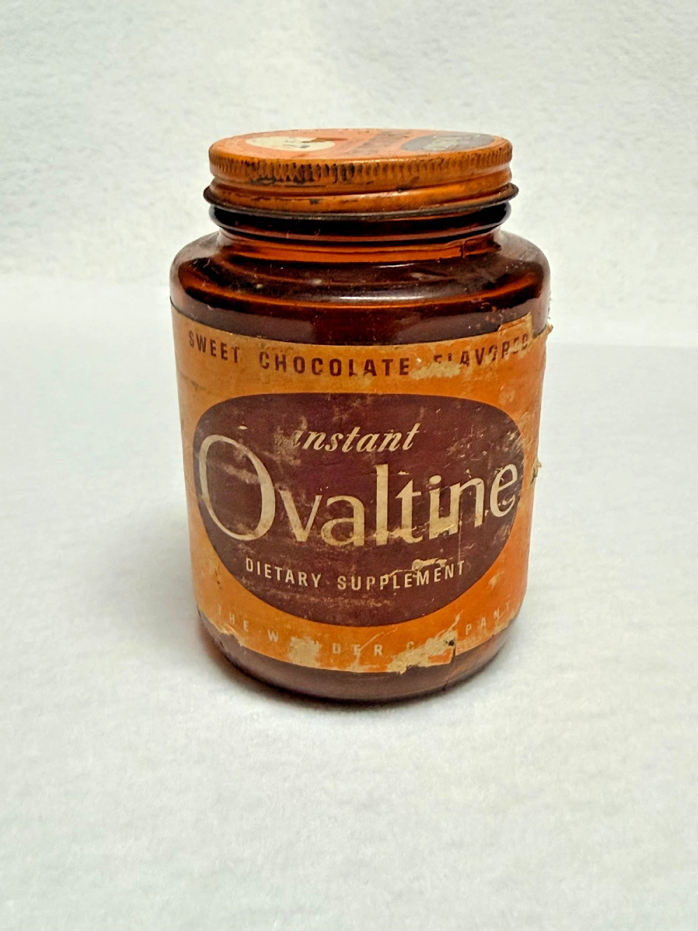 Vintage brown glass jar of instant Ovaltine dietary supplement with a worn orange paper label.