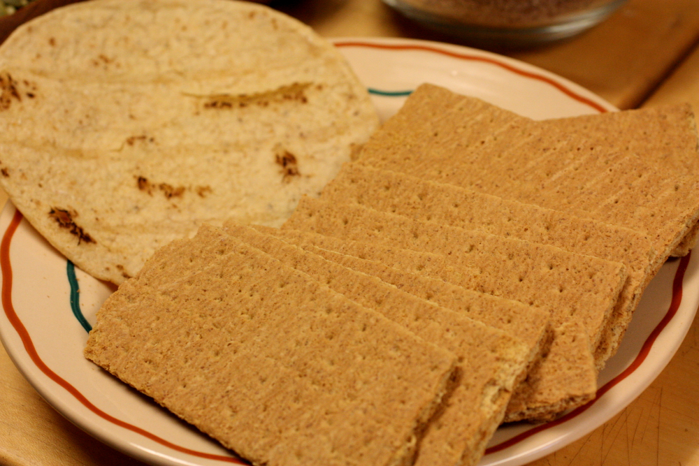 A round flatbread and several rectangular crispbread crackers on a plate.