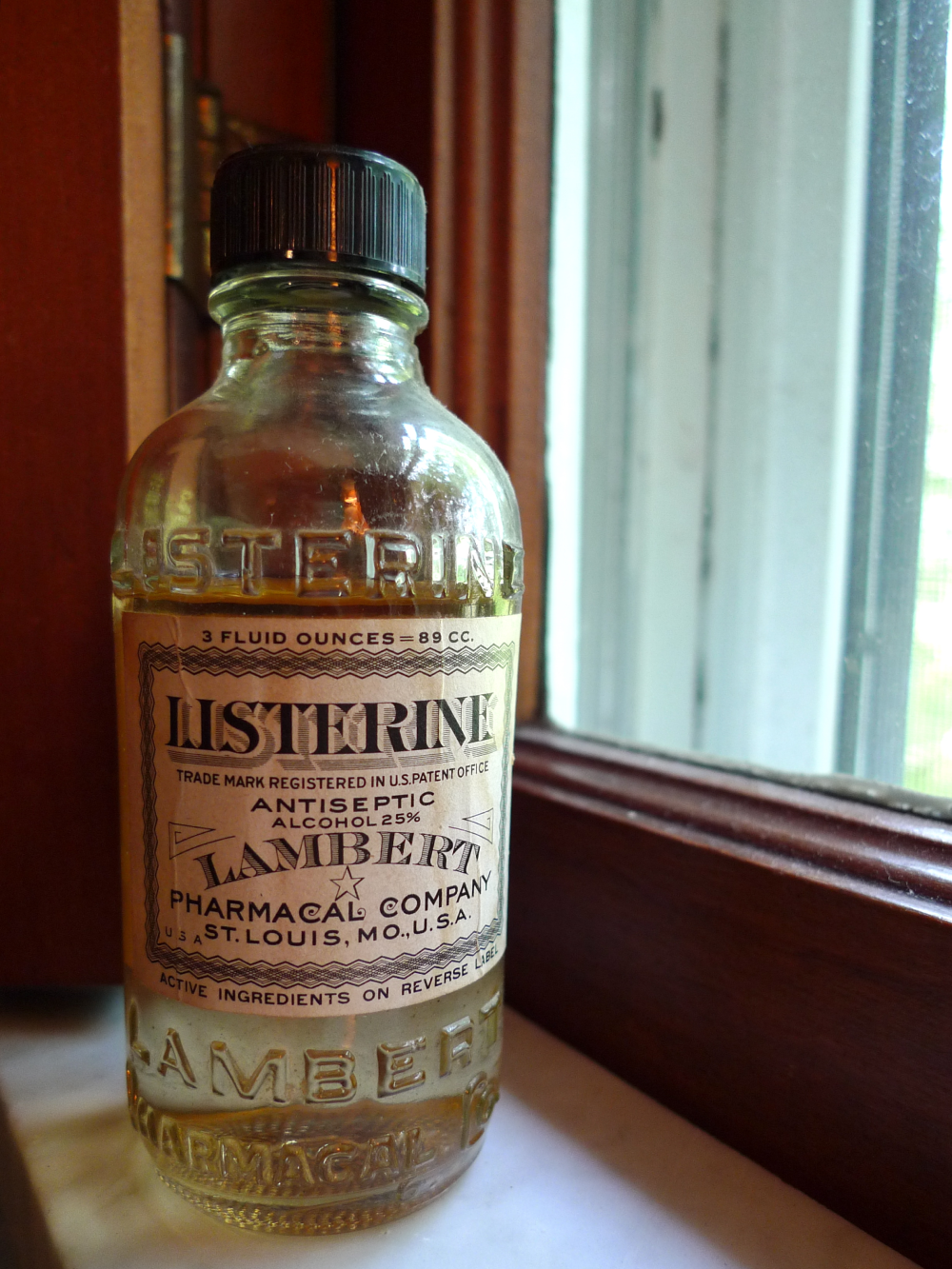 Vintage glass bottle of Listerine antiseptic with a black cap, sitting on a windowsill.