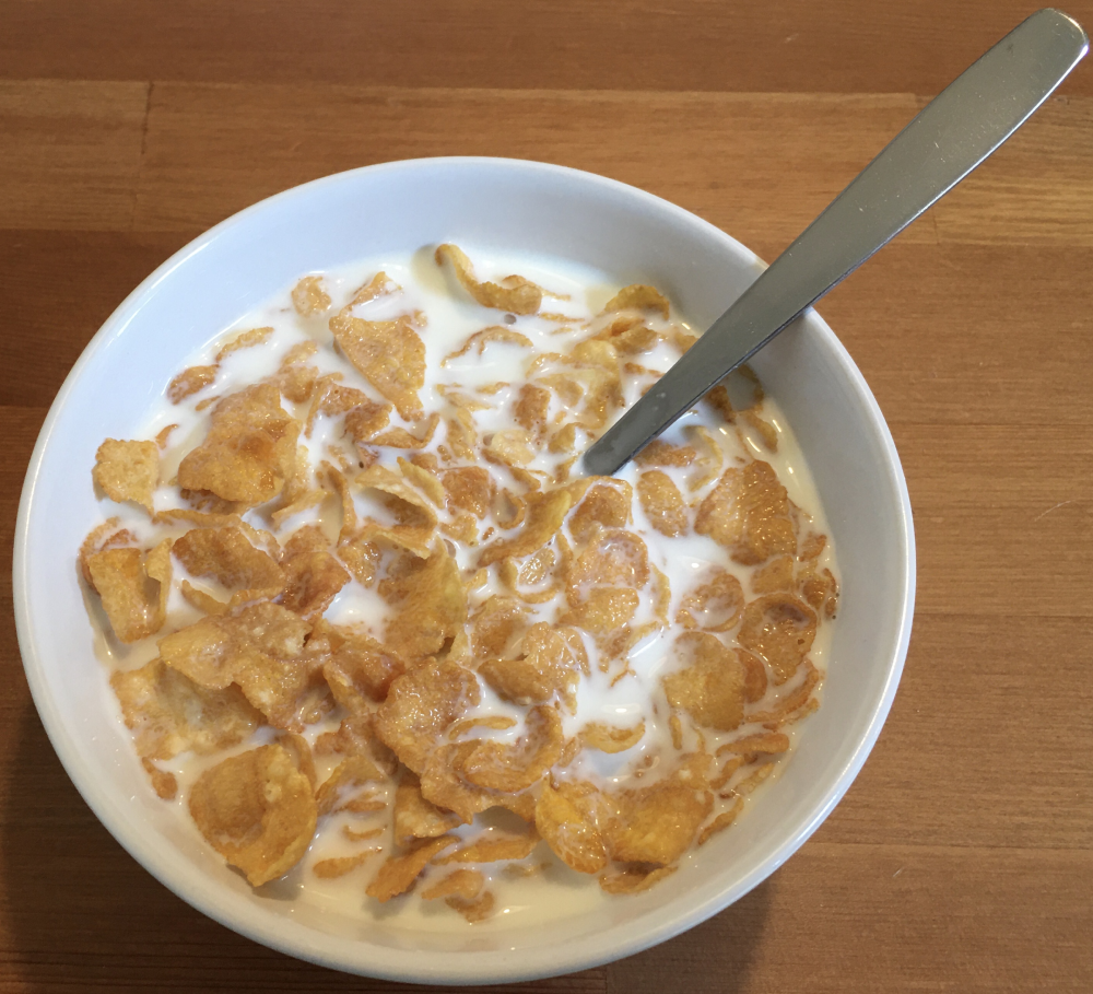 A bowl of cornflakes in milk with a spoon.