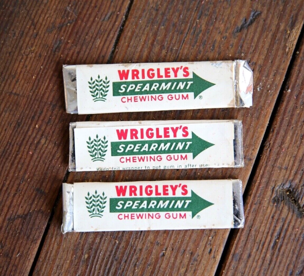 Three sticks of Wrigley’s Spearmint chewing gum arranged vertically on a wooden surface.