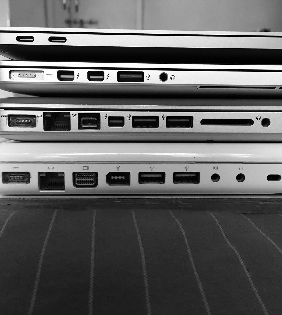 A stack of four laptops shown from the side, highlighting the variety of ports and connectors on their edges.