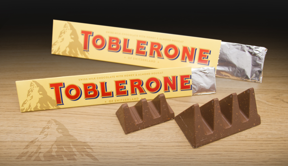 Two Toblerone chocolate bars in yellow packaging with two triangular chocolate segments placed in front.