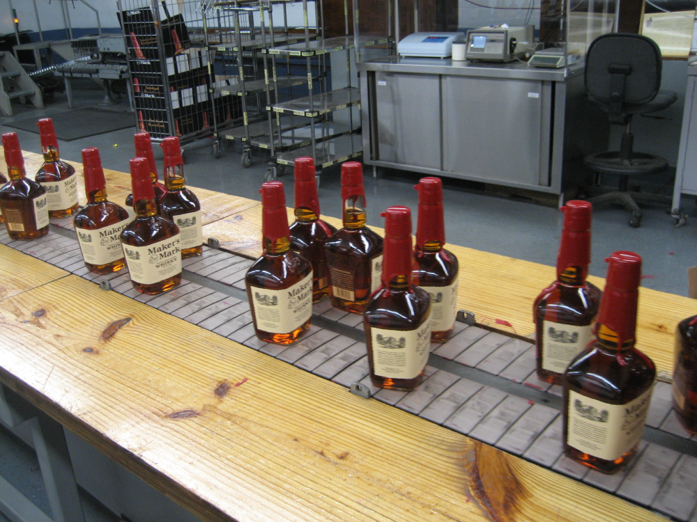 Bottles of Maker’s Mark whisky with signature red wax seals moving along a factory conveyor belt.