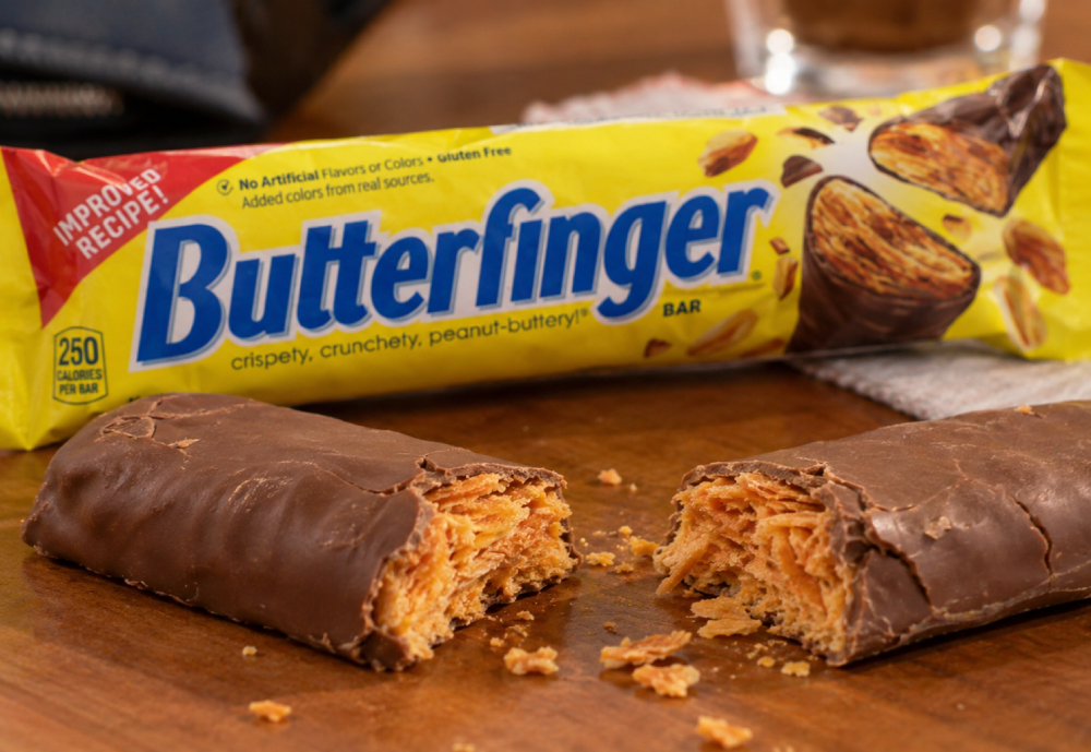 A Butterfinger candy bar broken into two pieces on a wooden surface, with the original yellow packaging in the background.