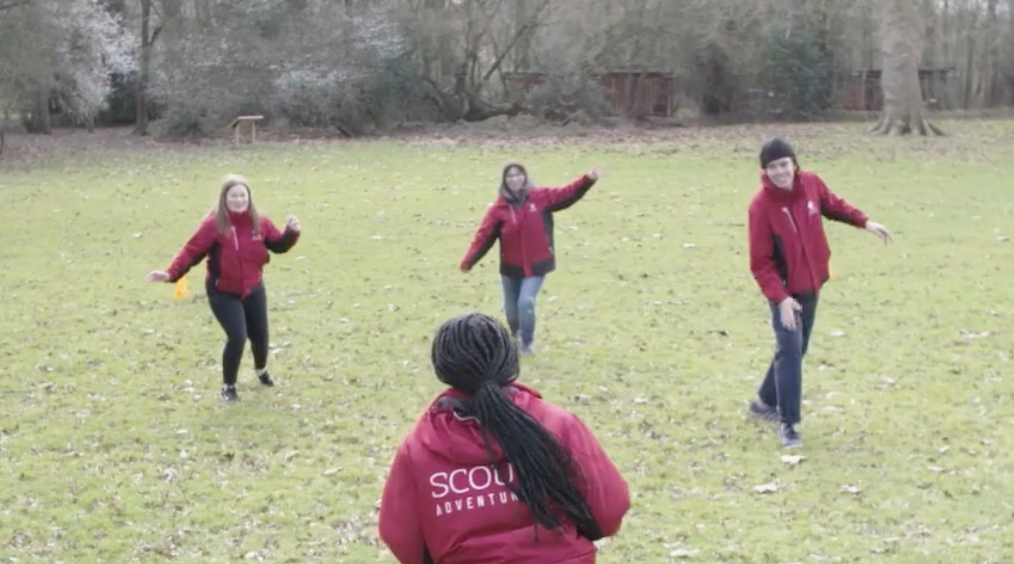 Four people in red Scout Adventure jackets standing in a grassy field.