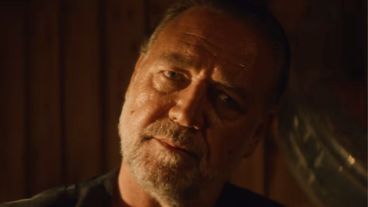 A middle-aged man with a beard and mustache looks thoughtfully at the camera, illuminated by warm, soft lighting with a wooden background.