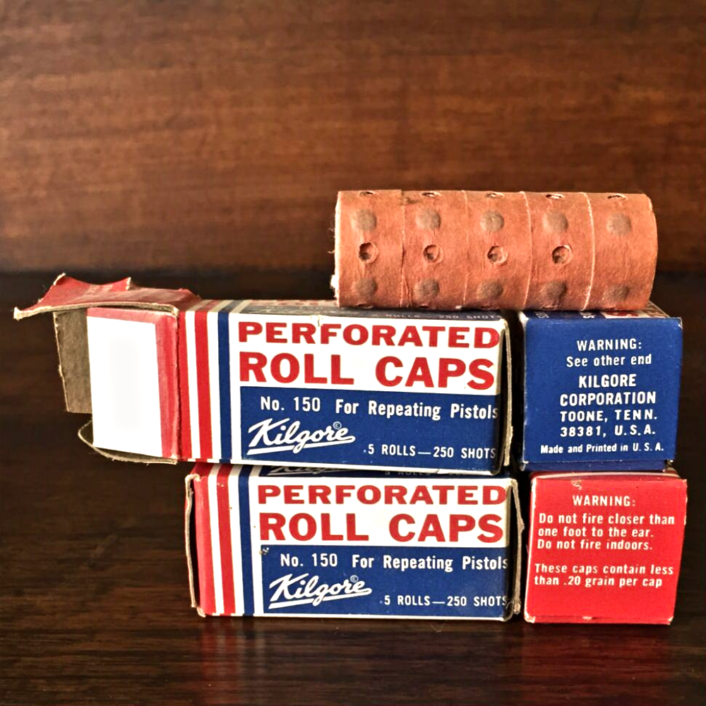 Two boxes of Kilgore brand perforated roll caps for toy pistols, with a roll of caps resting on top.