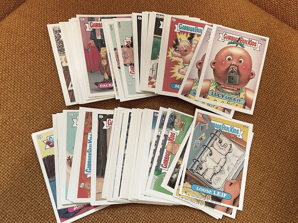 A fan of vintage Garbage Pail Kids trading cards fanned out on a textured surface.
