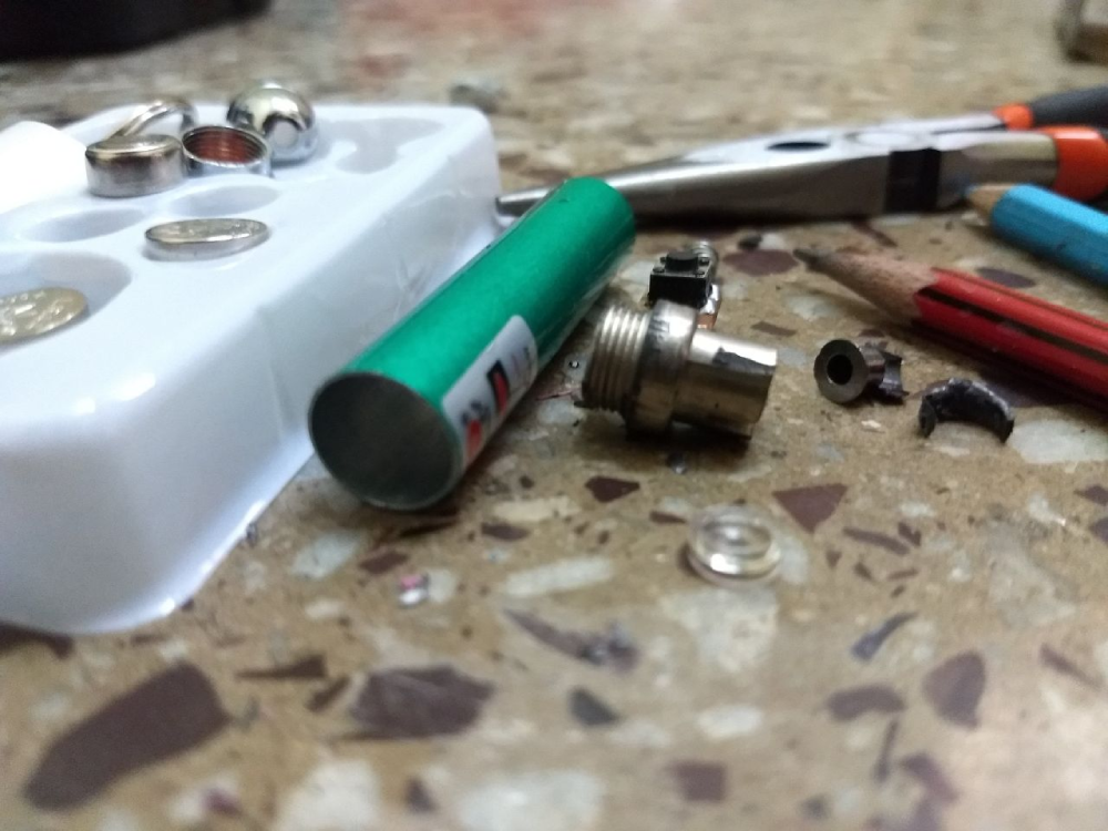A disassembled green laser pointer, small internal components, pliers, and a pencil scattered on a speckled surface.