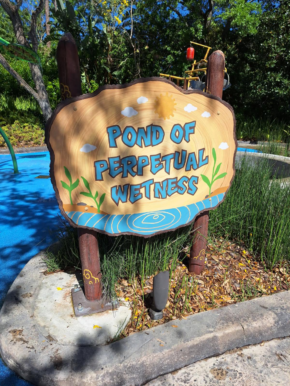 A sign at a water park reads “Pond of Perpetual Wetness” with illustrations of a sun, clouds, and plants.