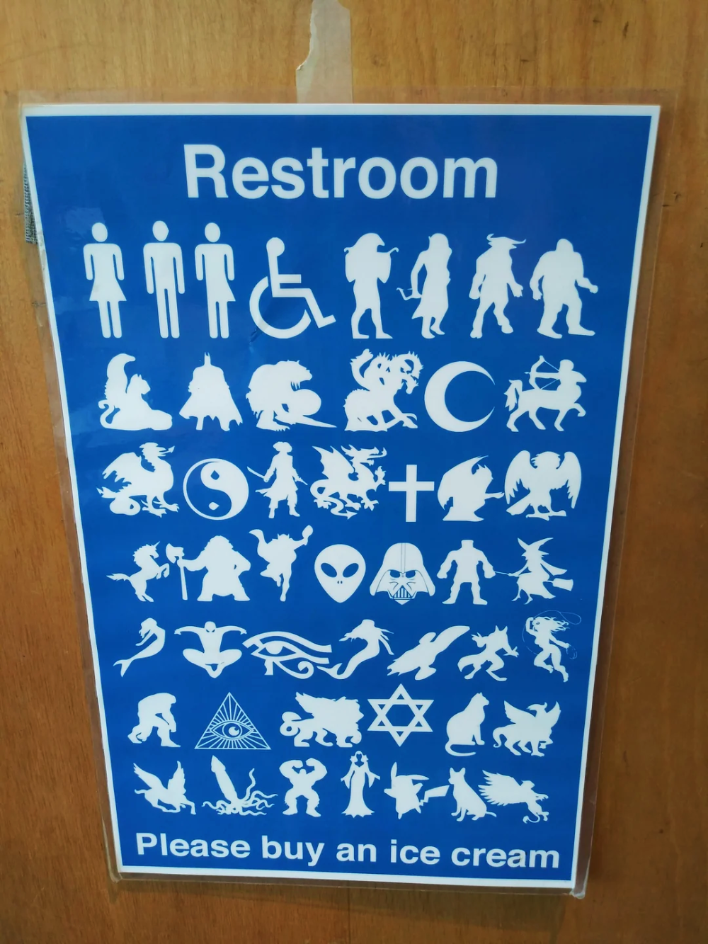 Blue sign labeled “Restroom” featuring rows of icons depicting people, mythological creatures, religious symbols, and pop culture characters, with the text “Please buy an ice cream” at the bottom.
