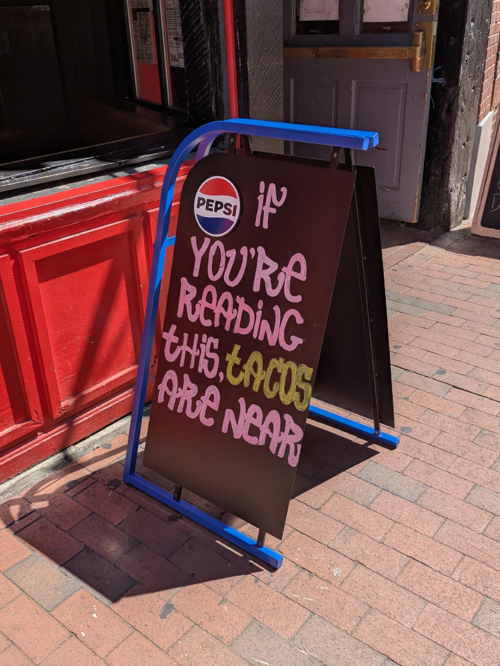 A sidewalk sandwich board sign with a Pepsi logo that reads, “If you’re reading this, tacos are near.”