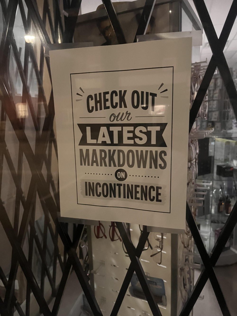 A sign taped to a window that reads, “Check out our latest markdowns on incontinence.”
