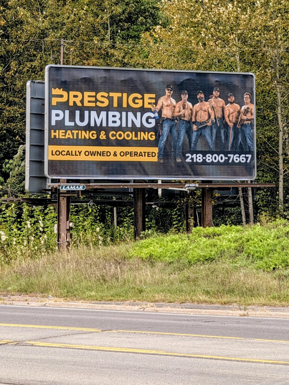 Billboard for Prestige Plumbing, Heating & Cooling featuring six shirtless men holding plumbing tools, with a phone number and “Locally owned & operated” text.