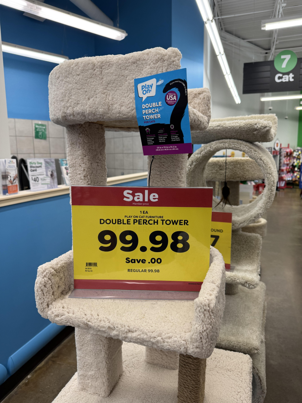 A beige carpeted cat tower with a sale sign reading “Double Perch Tower” for $99.98.