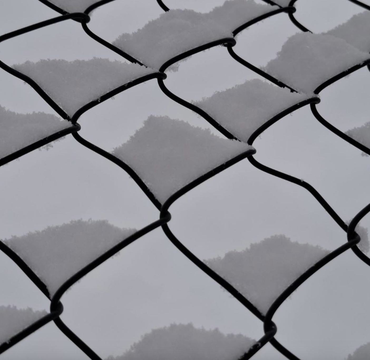 A close-up of a chain-link fence covered in patches of snow.