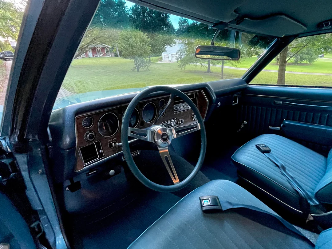 Interior view of a vintage car with a wood-grain dashboard, three-spoke steering wheel, and blue vinyl bench seats.