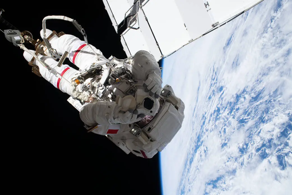 An astronaut in a spacesuit tethered to the International Space Station during a spacewalk, with Earth visible in the background.