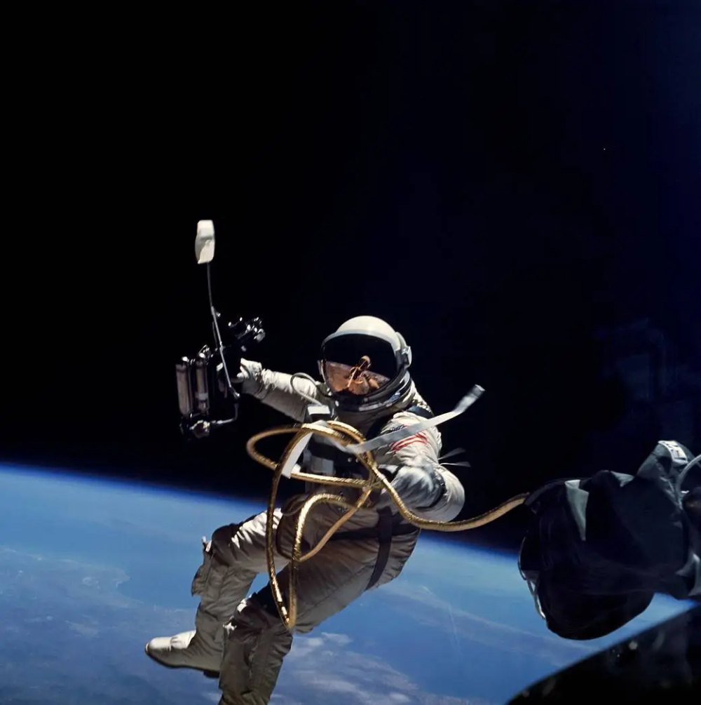 An astronaut floats in space, tethered to a spacecraft, with the Earth visible in the background.