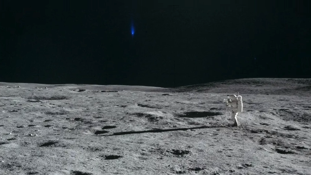 An astronaut in a spacesuit stands on the cratered lunar surface, photographing the landscape.