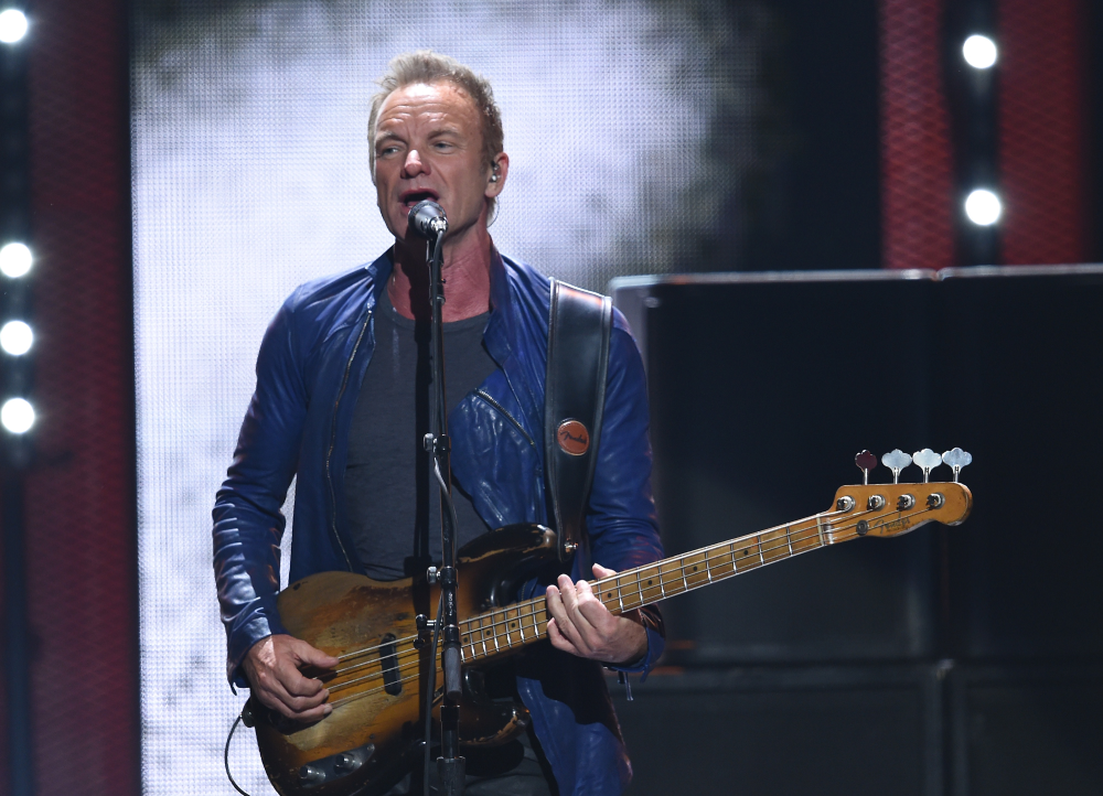 Sting singing into a microphone while playing a vintage Fender bass guitar on stage.