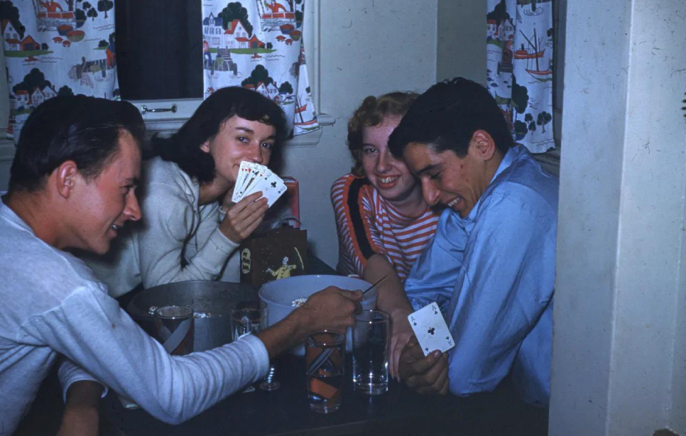 Four young people sit around a table playing cards and eating popcorn.