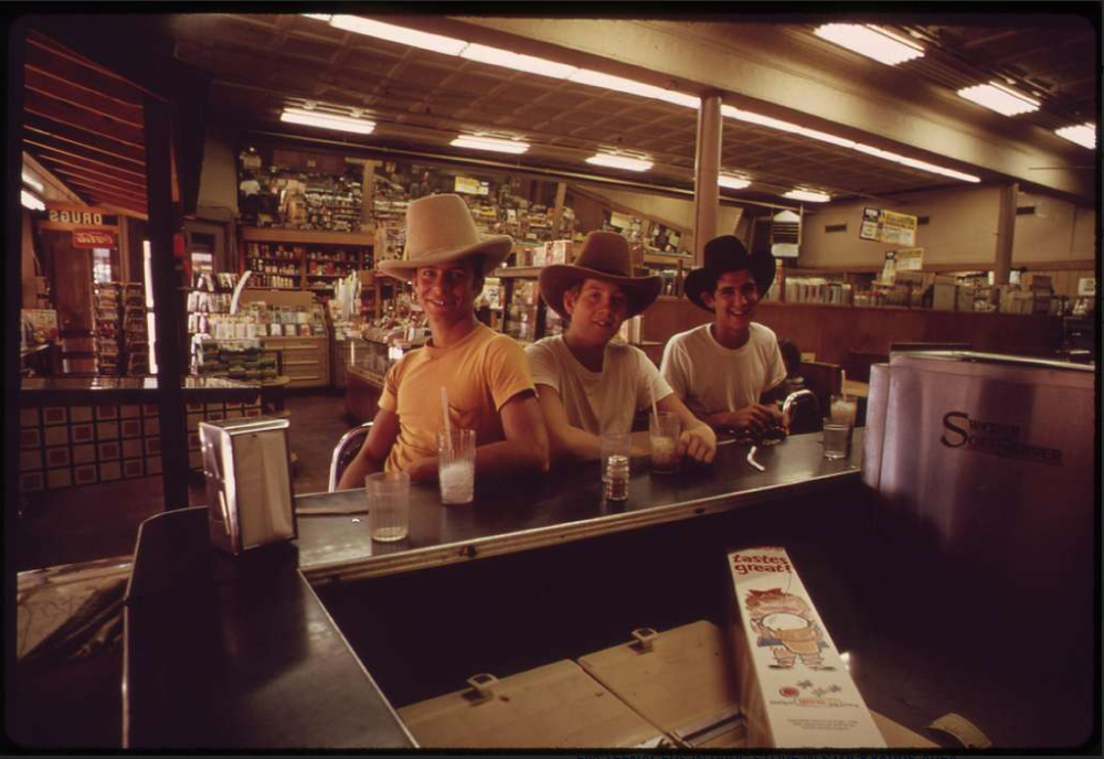 Three young men wearing cowboy hats sit at a diner counter with glasses of water.