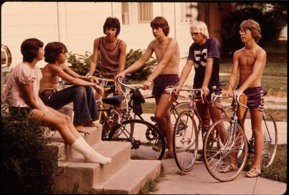 A group of six teenagers with bicycles gathered on and around the front steps of a house.