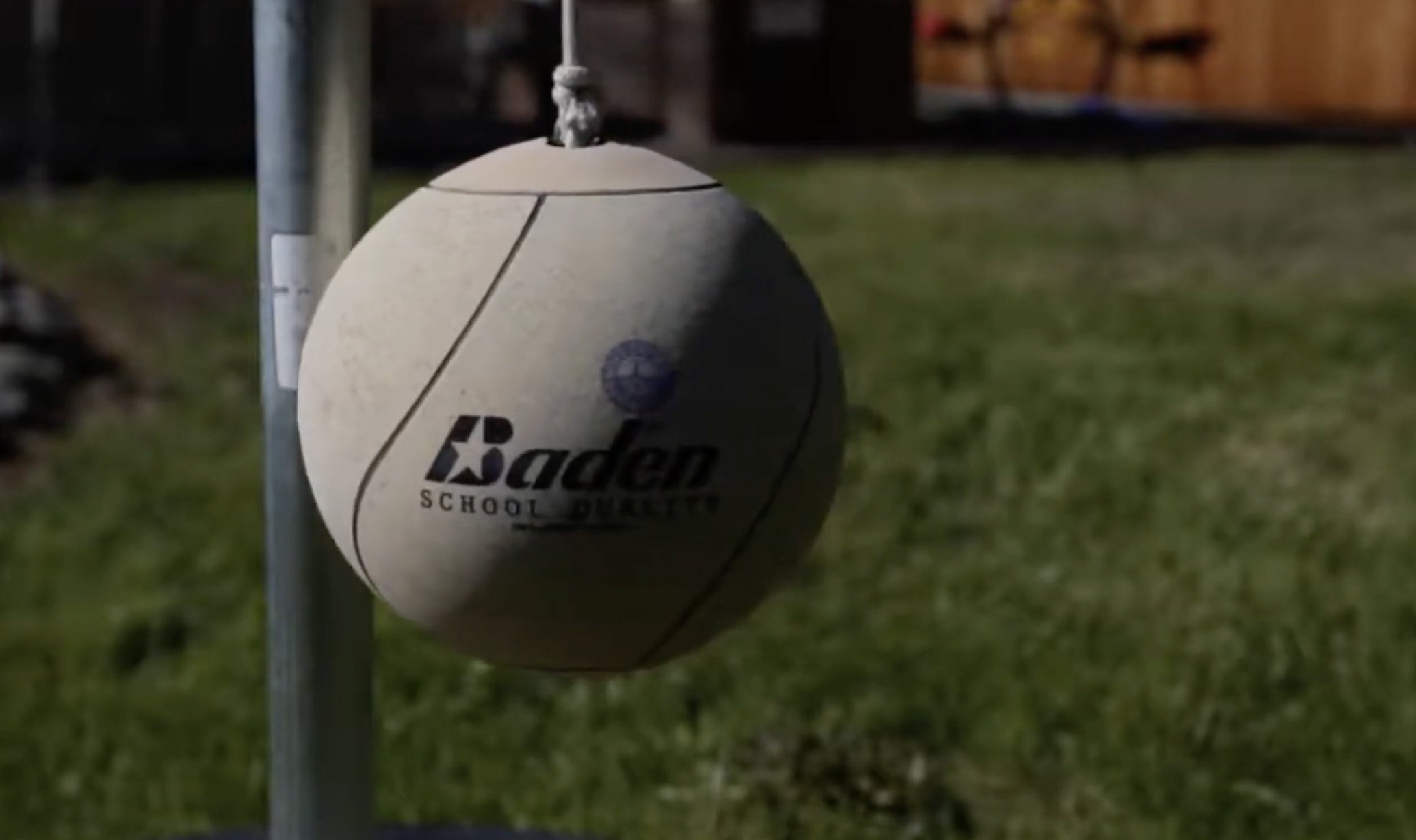 A Baden tetherball hanging from a metal pole outdoors.