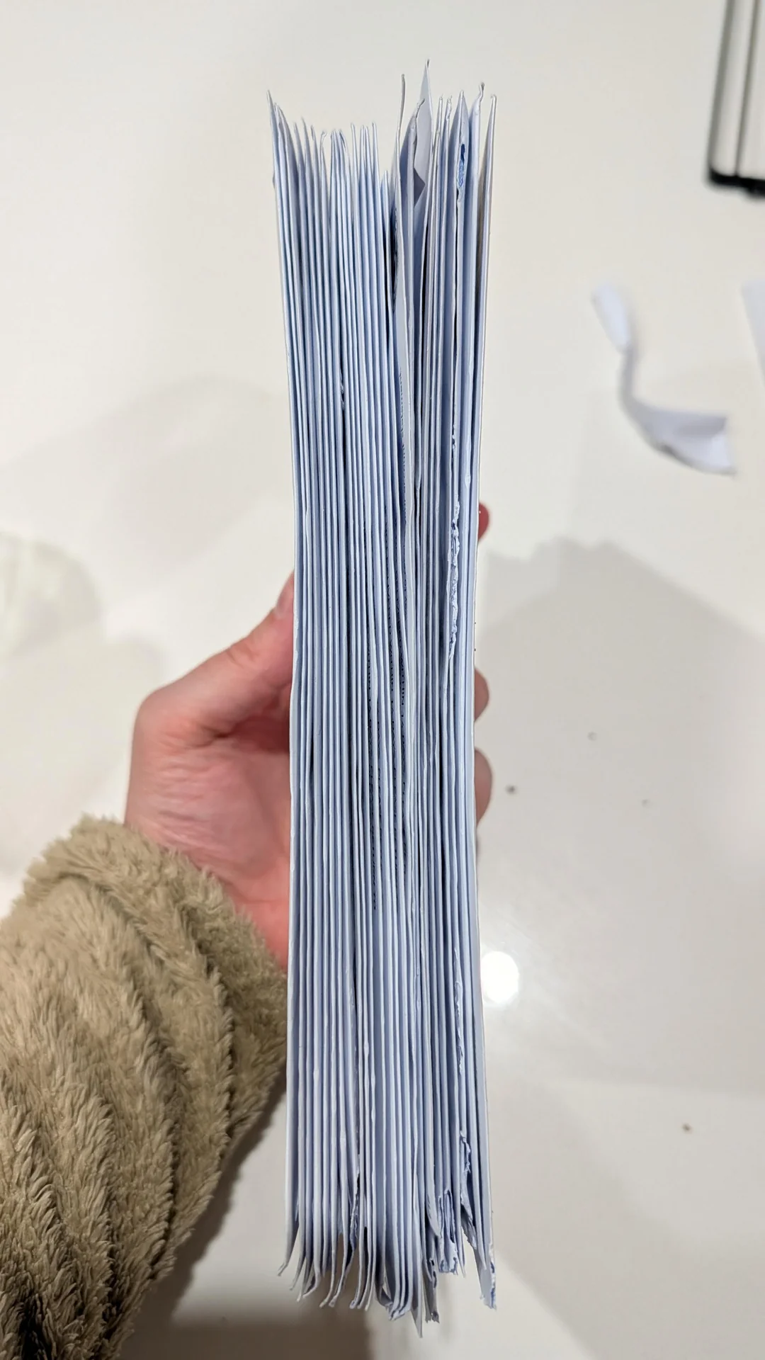 A hand holding a thick stack of folded white documents.