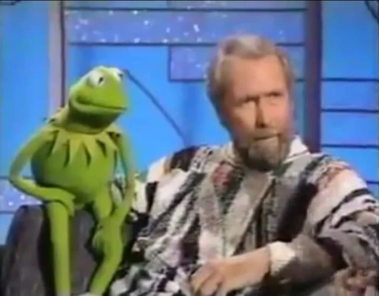 Jim Henson sitting next to Kermit the Frog on a television set.