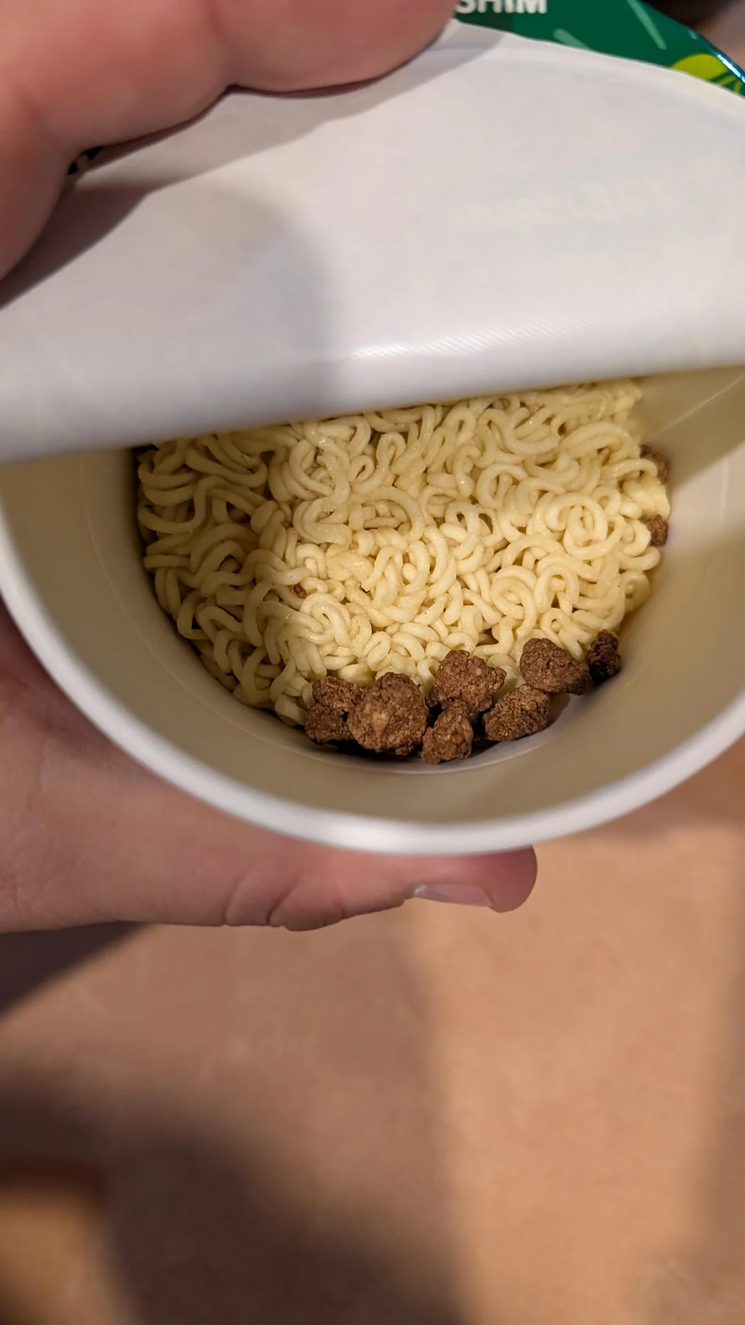 An open cup of dry instant noodles with small, brown seasoning clusters.