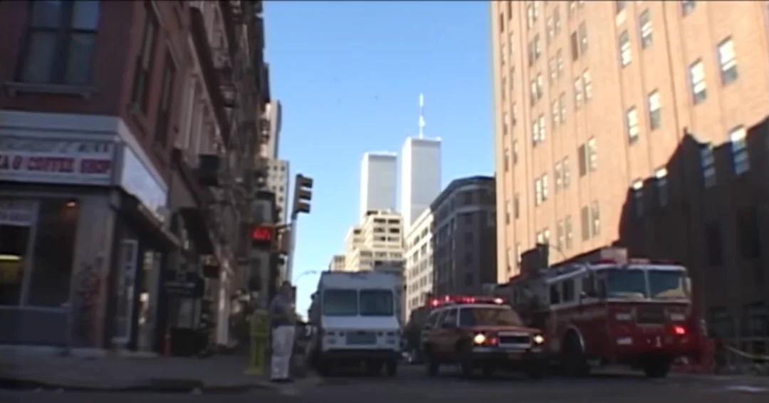 A view from a city street looking toward the Twin Towers, with a fire truck and emergency vehicle parked in the road.