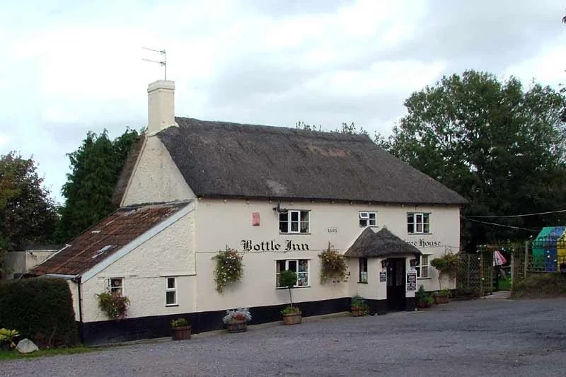 The Bottle Inn, a white building with a thatched roof and a gravel parking lot.