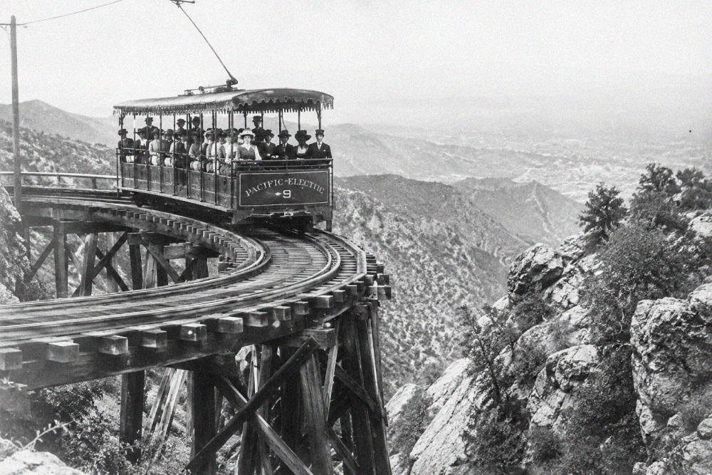 A Pacific Electric passenger trolley car travels along a high wooden trestle bridge overlooking a mountain canyon.