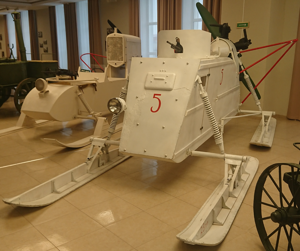 Two white, vintage motorized snow sleds with mounted machine guns displayed in a museum.