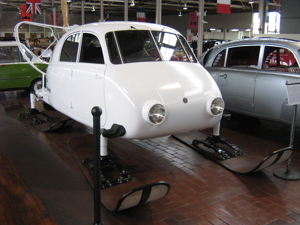 A white, pod-shaped experimental vehicle mounted on three large skis, displayed in a museum.