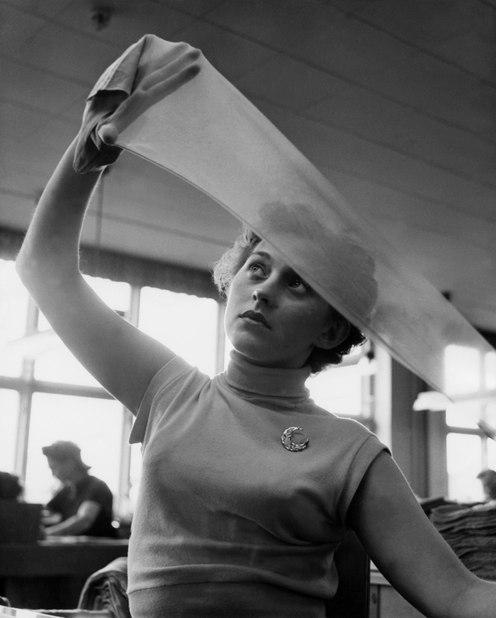 A woman holding a sheer fabric up to the light to inspect it.