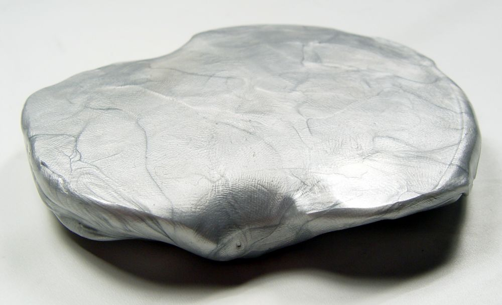 A flattened, irregular lump of silver metallic modeling clay.
