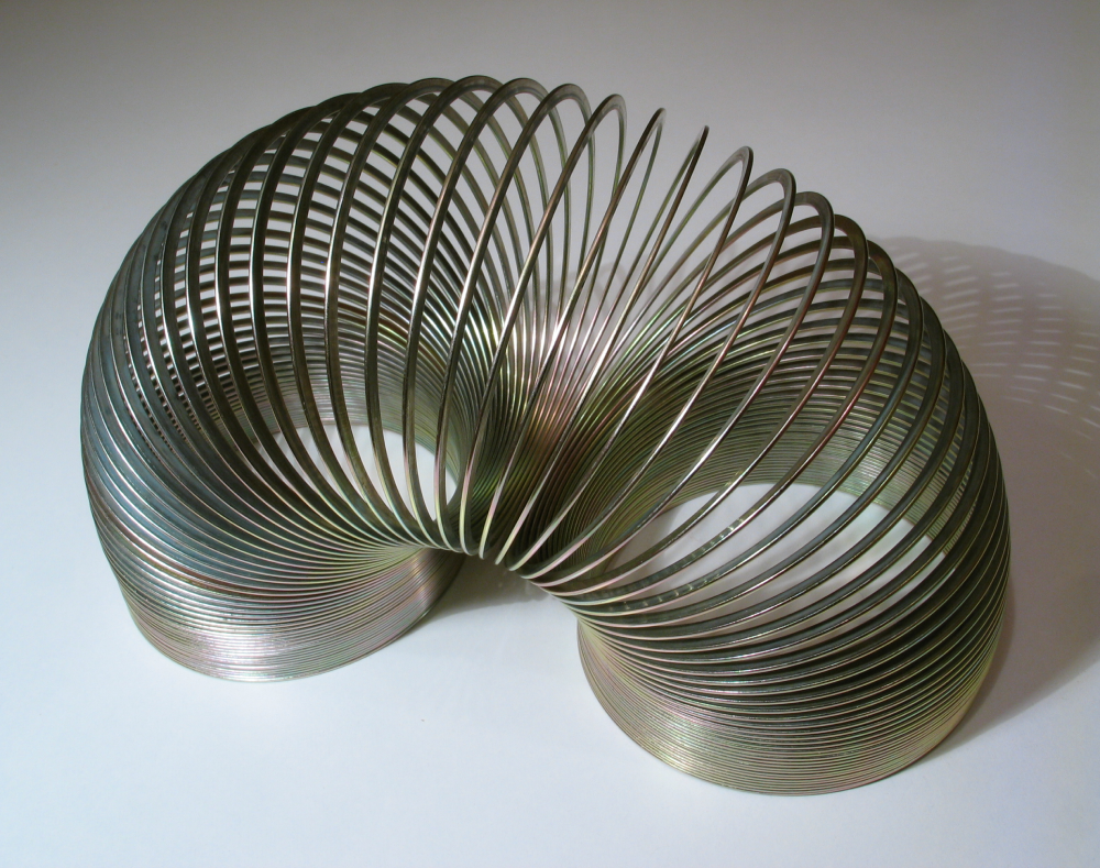 A metallic coil toy arched on a white surface.