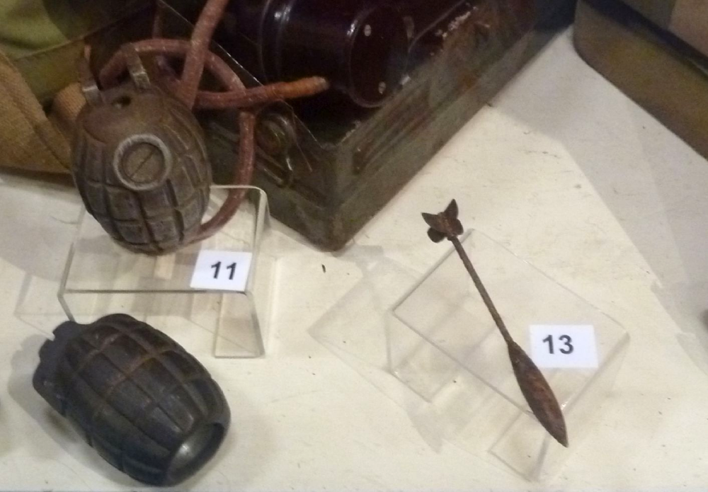 Two vintage hand grenades and a small metal dart displayed on museum pedestals numbered 11 and 13.