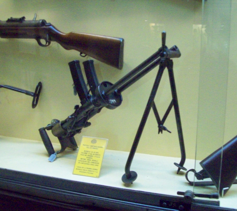 A Villar Perosa submachine gun on a tripod displayed inside a glass museum case.