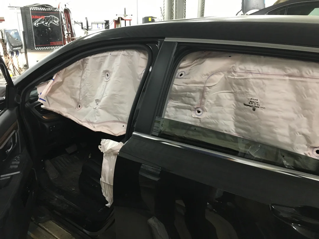 Side-curtain airbags deployed inside a black car with the windows down.