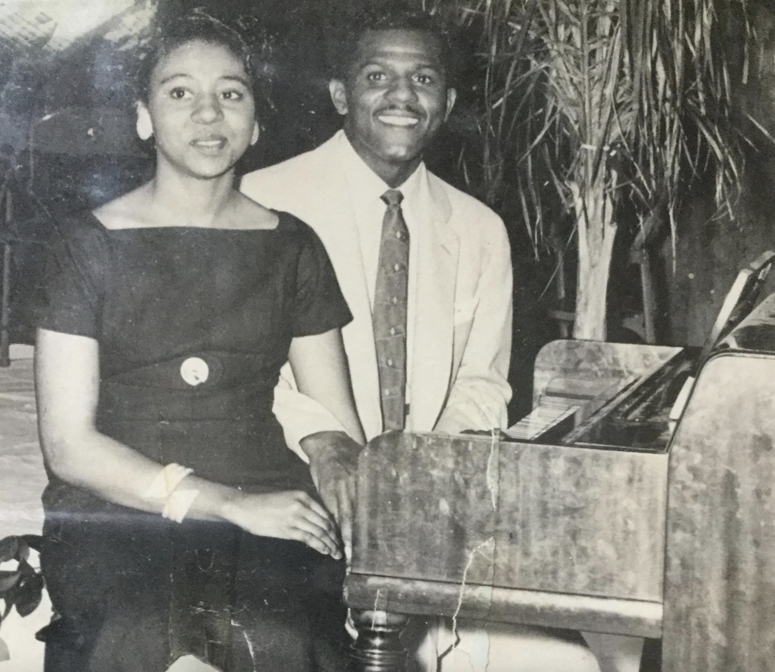 A young man and woman sitting together at a piano in a vintage black and white photograph.